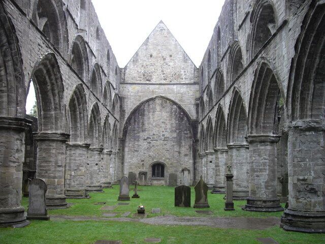 An ancient cloister with arched walkways and tombstones.
