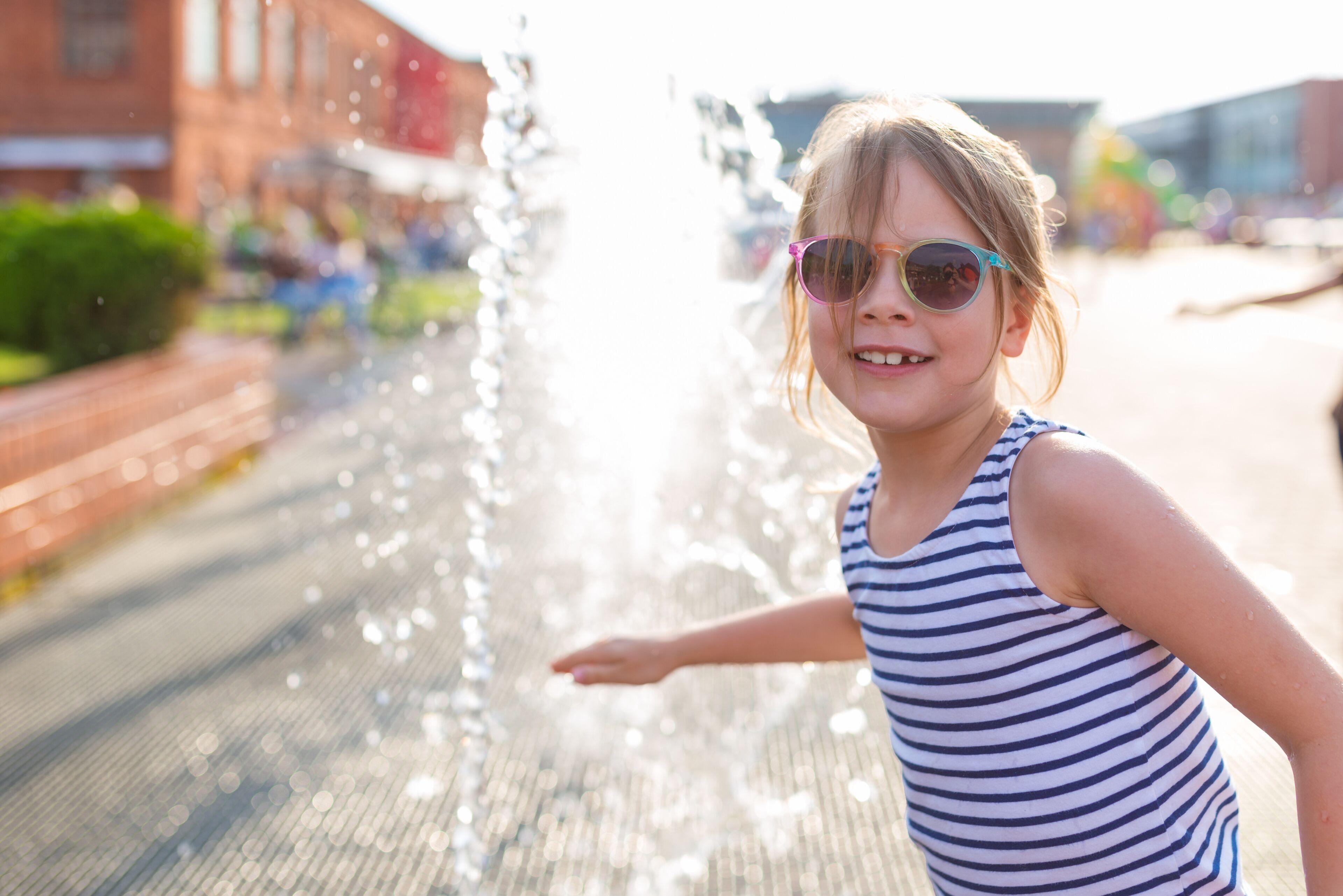 Little amused girl in sunglasses playing by the streams of the city fountain in Manufaktura in Lodz - Poland