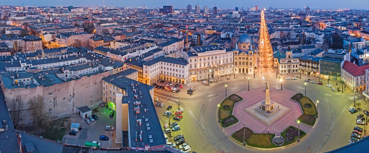 A cityscape at dusk with a prominent roundabout, historic buildings, and a central monument.