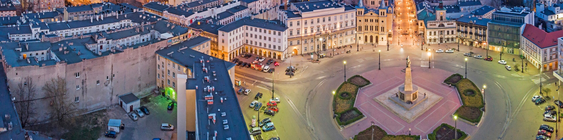A cityscape at dusk with a prominent roundabout, historic buildings, and a central monument.