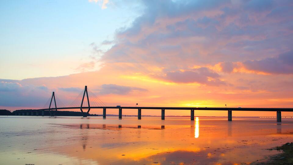 A sunset over a calm body of water with a bridge in the distance.