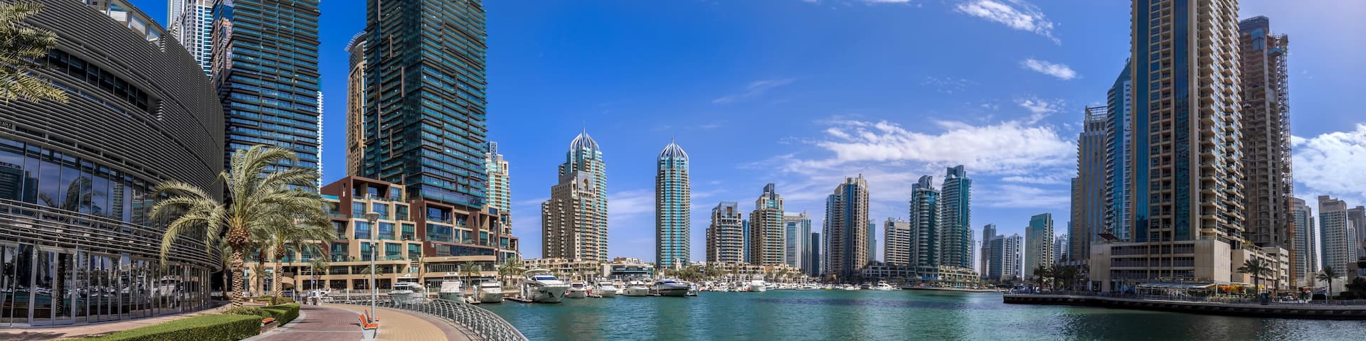 A marina with boats, tall modern buildings, and a clear blue sky.