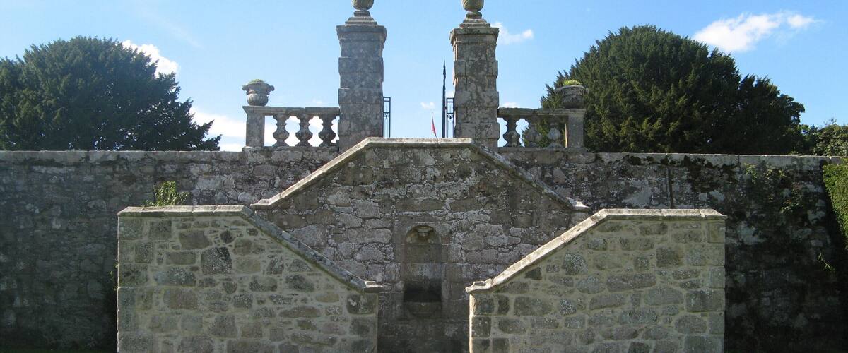 A stone structure with two towers and a central entrance, surrounded by a grassy area and trees.