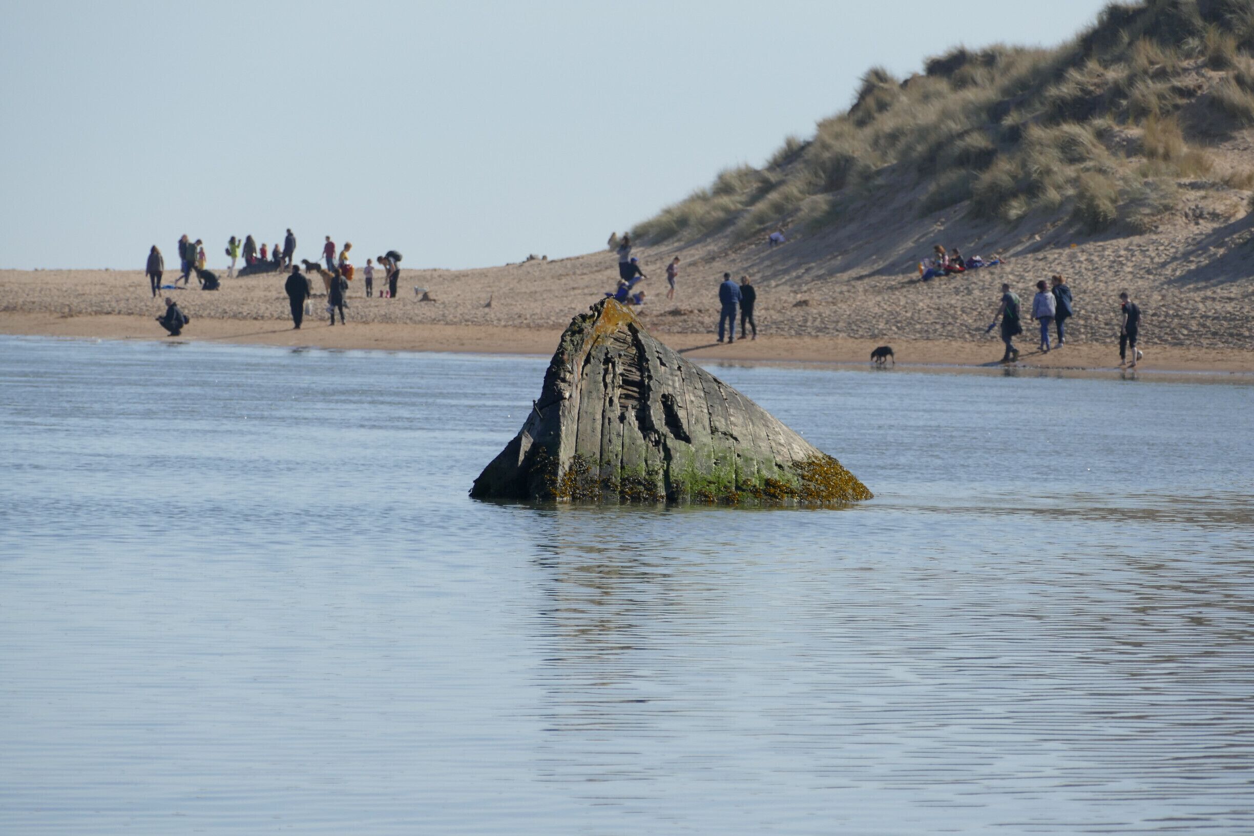 A large rock formation in the water with people on the beach in the background.