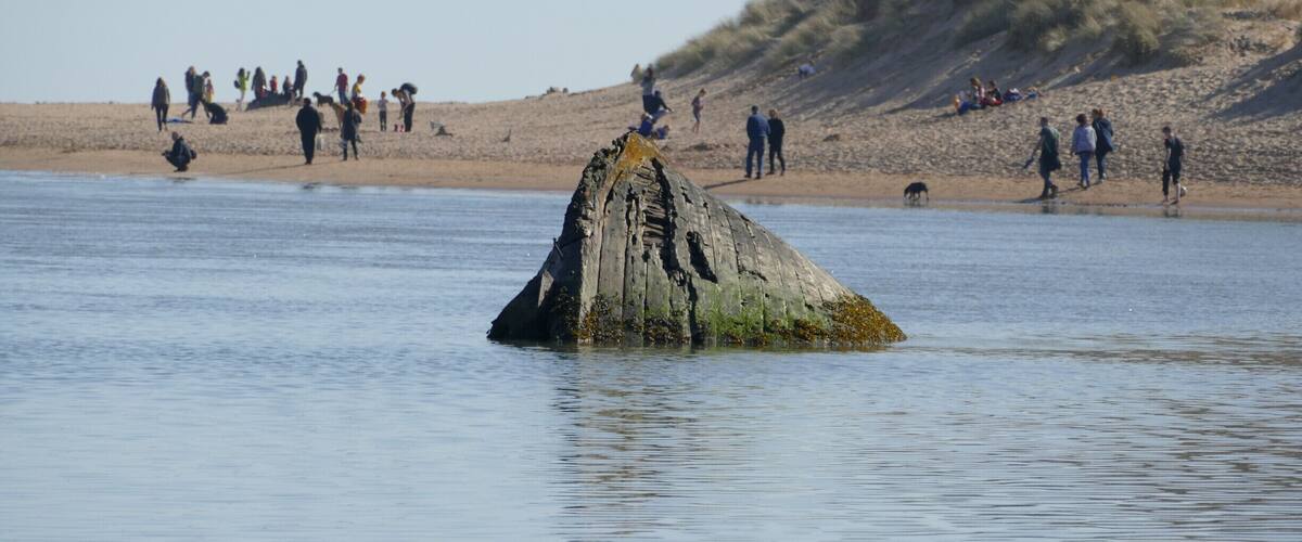 A large rock formation in the water with people on the beach in the background.