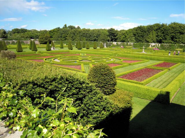 Un jardín formal con setos de formas geométricas y diversas especies de árboles.