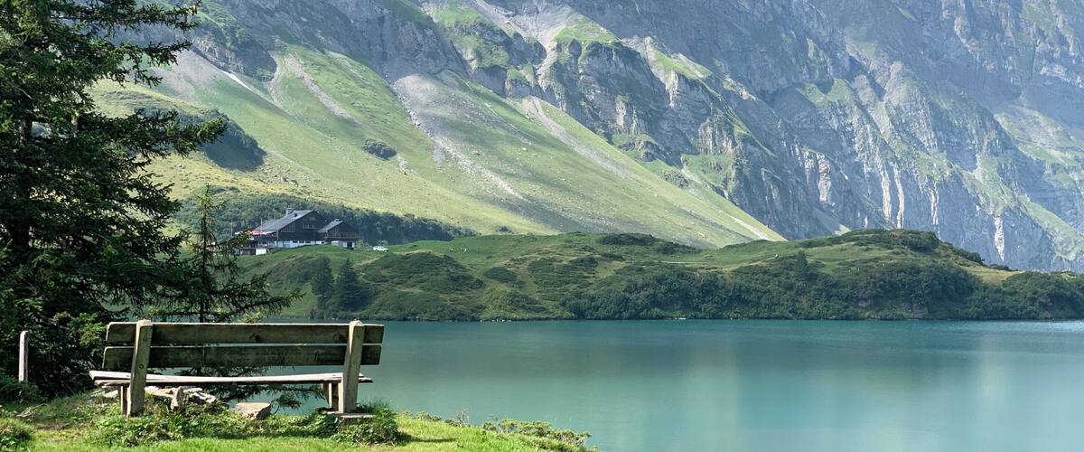 A lake with mountains in the background and a wooden bench in the foreground.