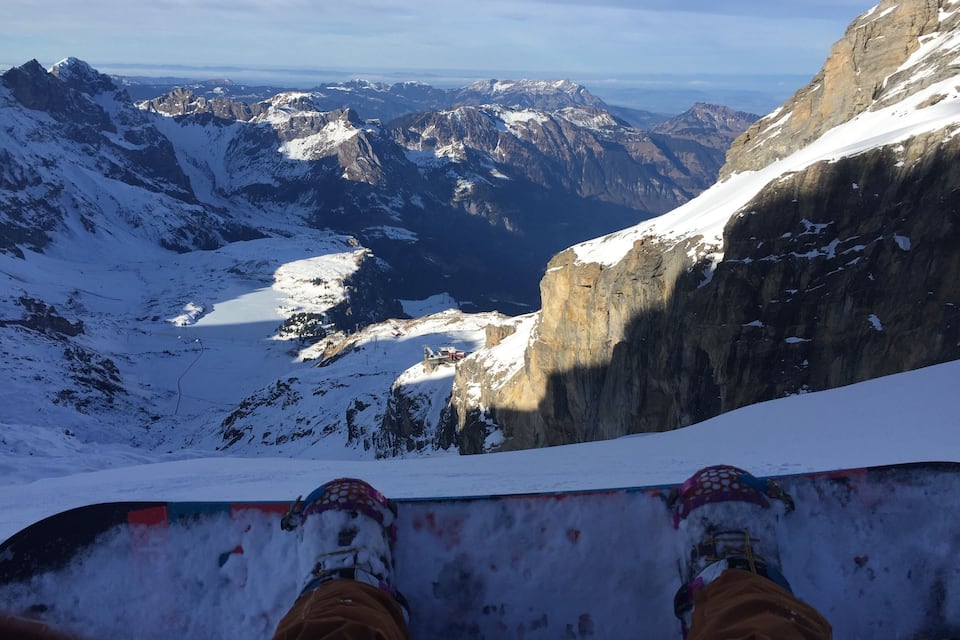A snowboarder's feet on a snowy slope with a mountain range in the background.
