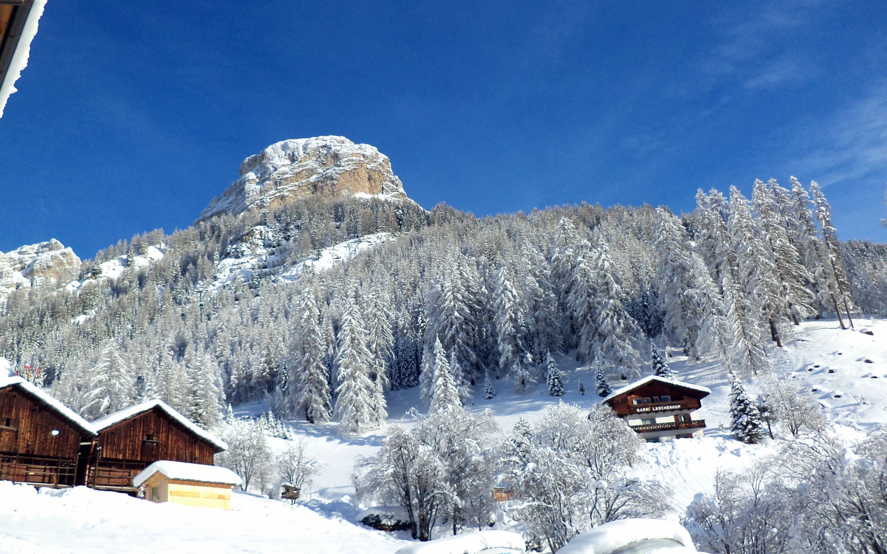 A snow-covered mountain with wooden cabins at its base.