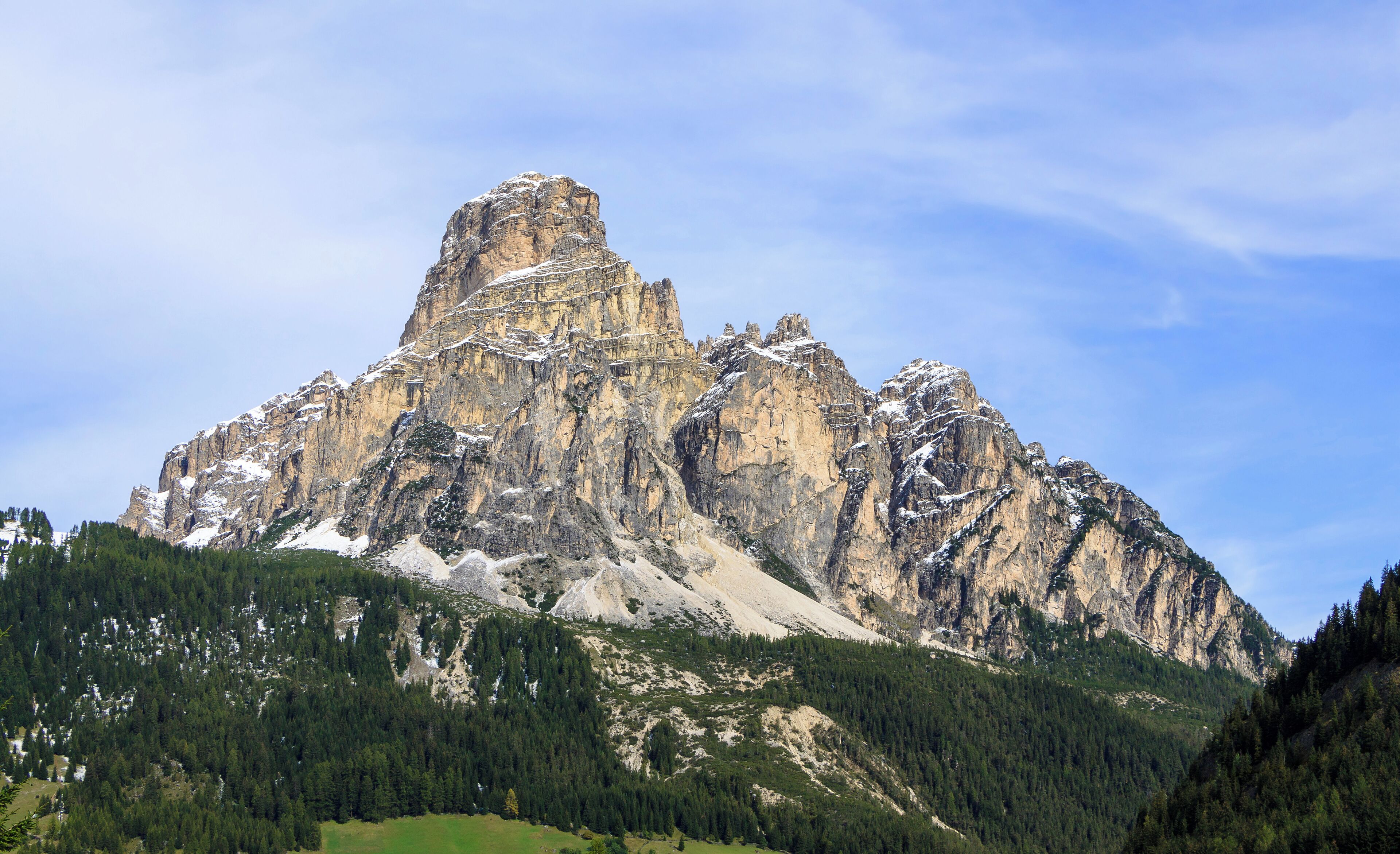 A rugged mountain peak with snow patches, surrounded by dense forest.