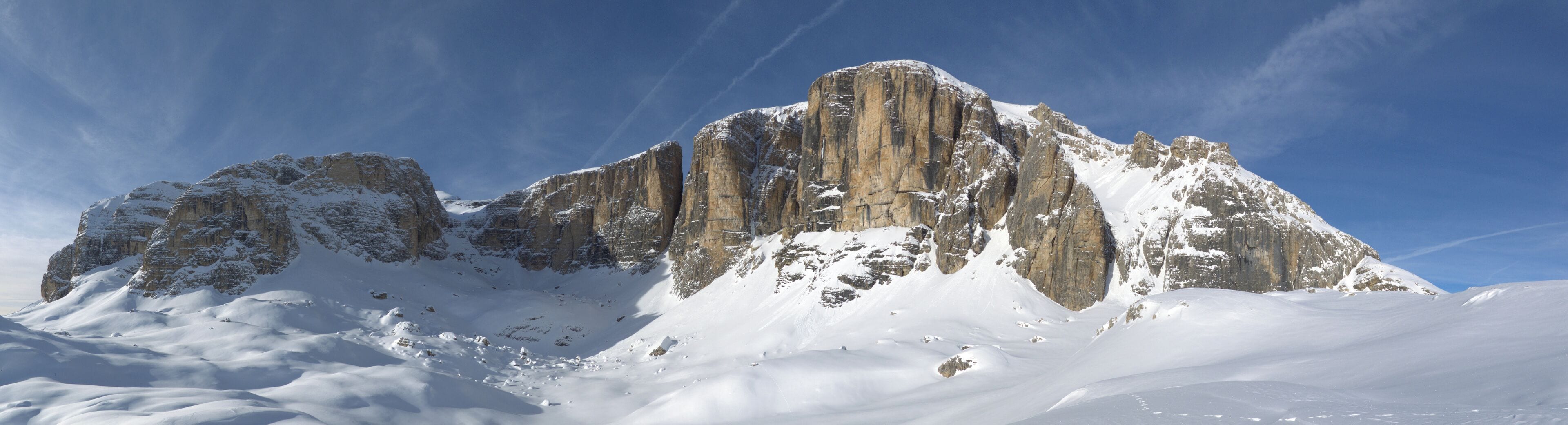 A snow-covered mountain peak with sharp, rugged cliffs and a clear blue sky.