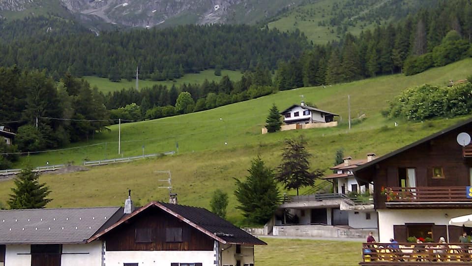 A mountainous landscape with a parking lot, buildings, and a house in the foreground.