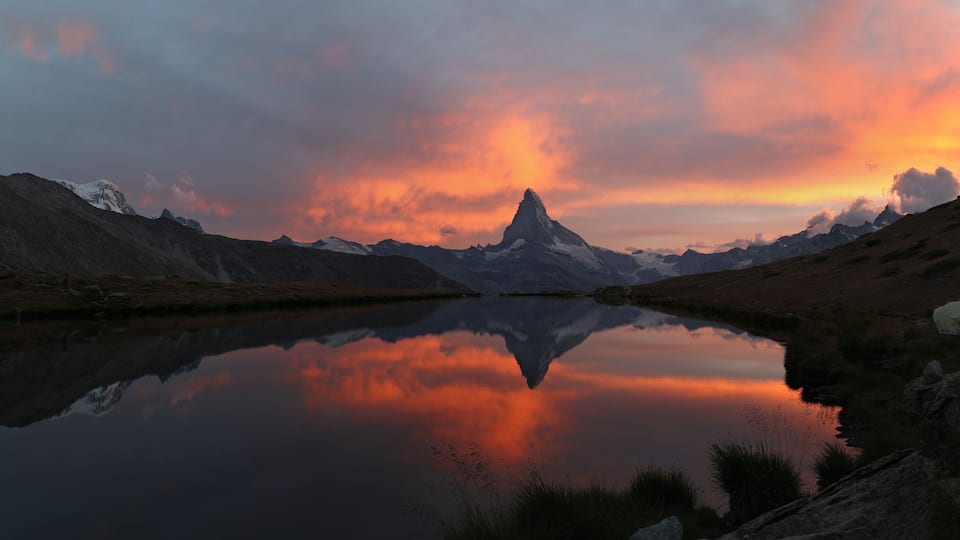 A mountain lake with a reflection of the sky, surrounded by rugged terrain.