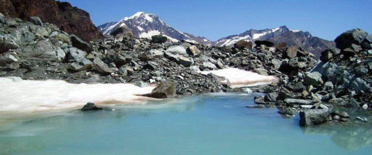 A glacial lake surrounded by rocky terrain and snow-capped mountains.