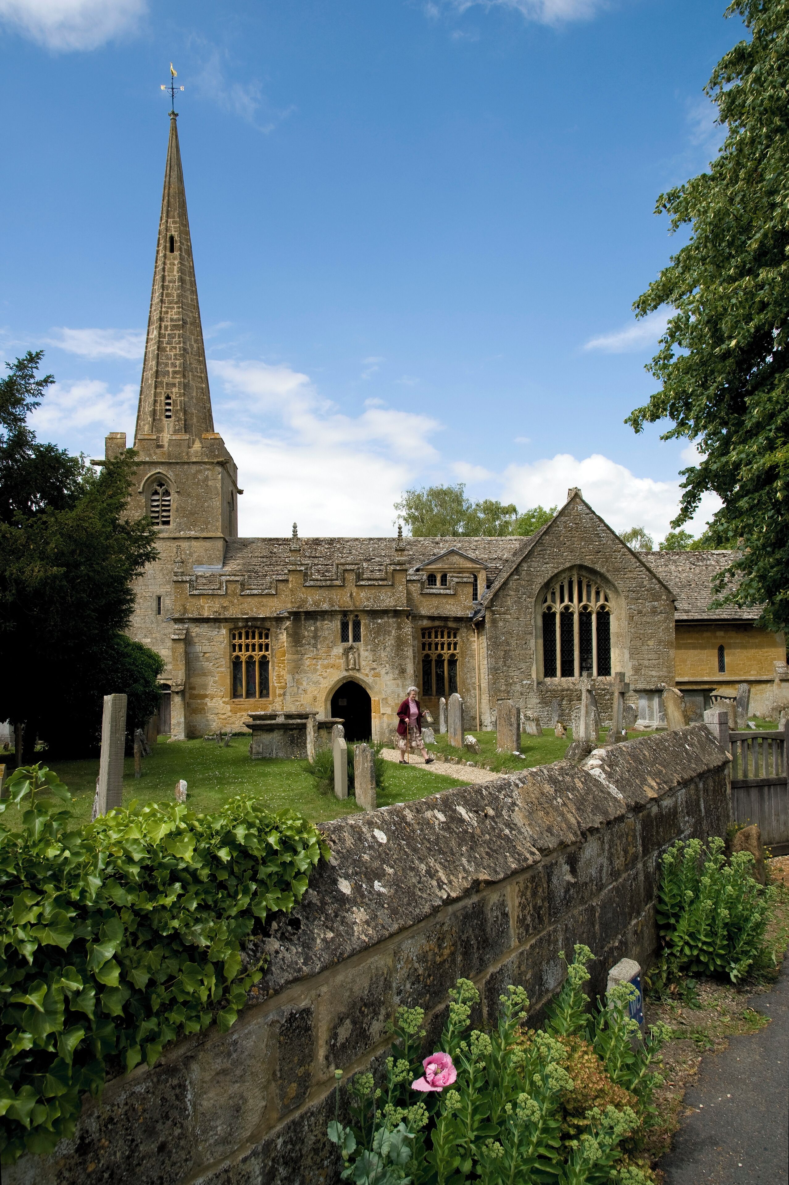 A historic church with a tall spire, a stone wall, and a cemetery.