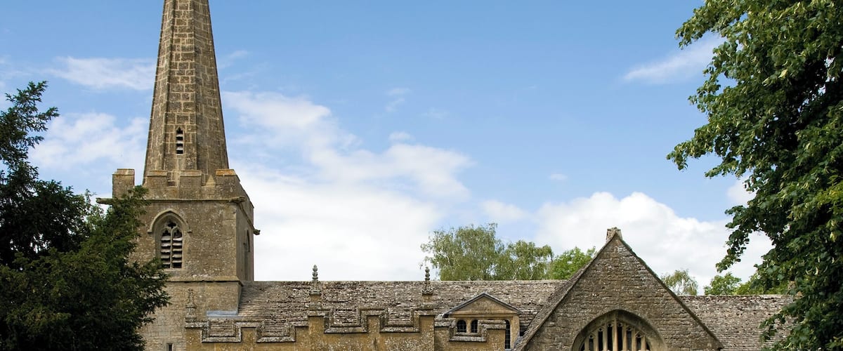 A historic church with a tall spire, a stone wall, and a cemetery.