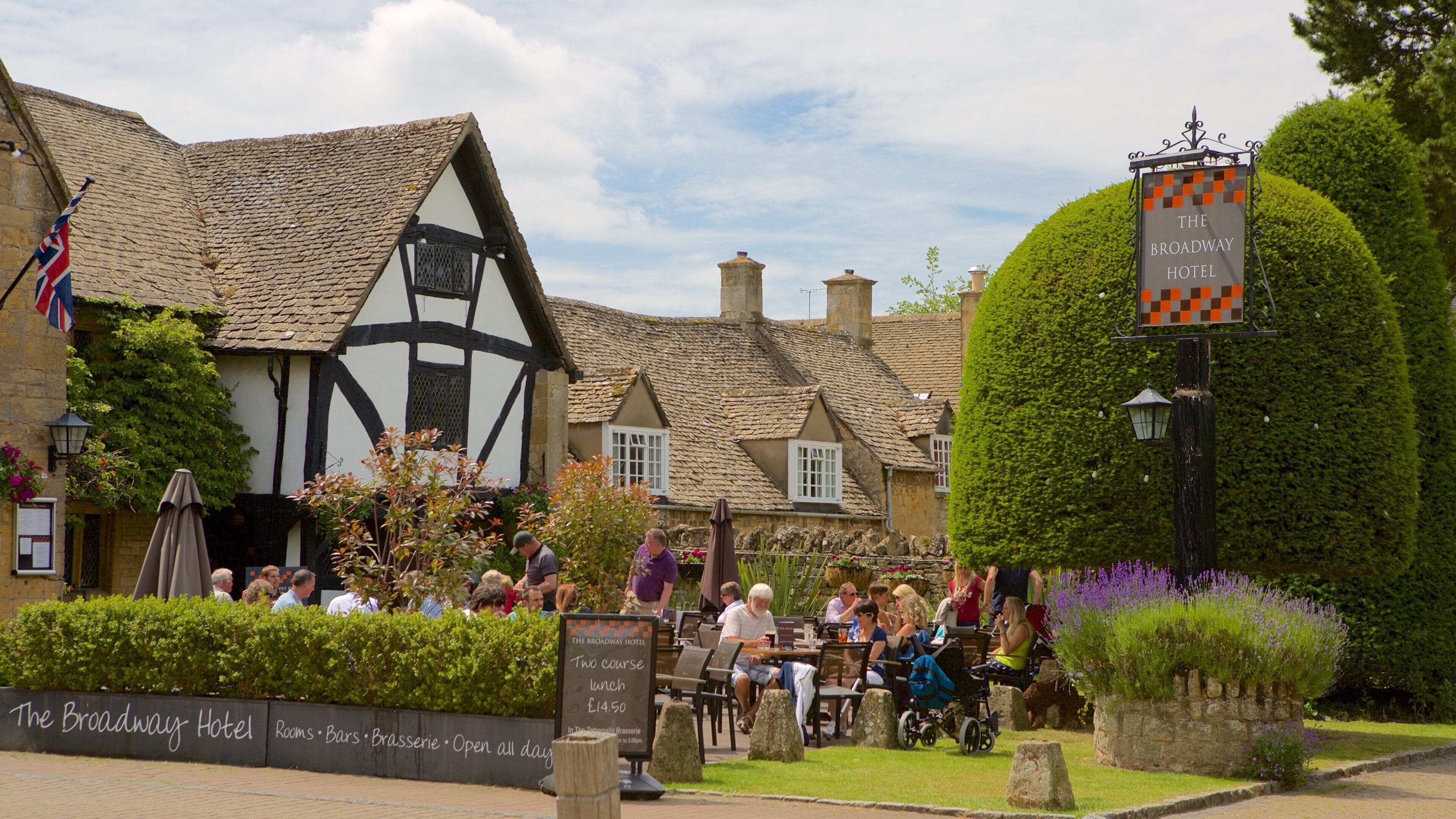 The Broadway Hotel with traditional Tudor-style architecture, outdoor seating, and a signboard advertising a lunch course.