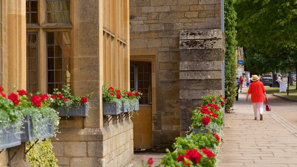 A stone building with red flowers in window boxes and a person walking on the sidewalk.