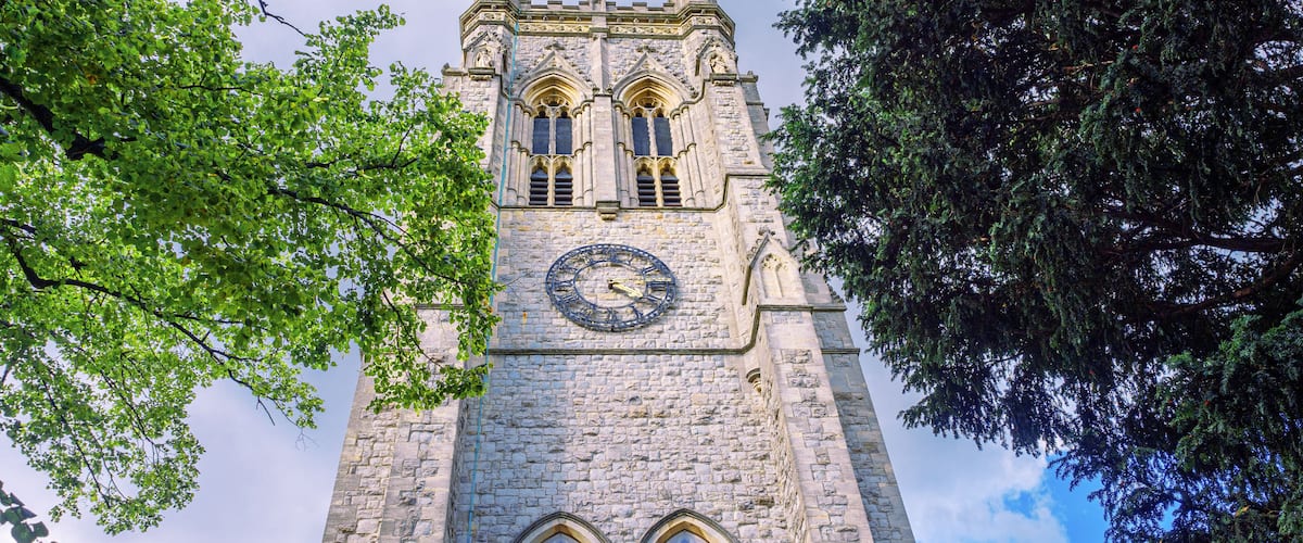 A tall stone tower with a clock, surrounded by trees.