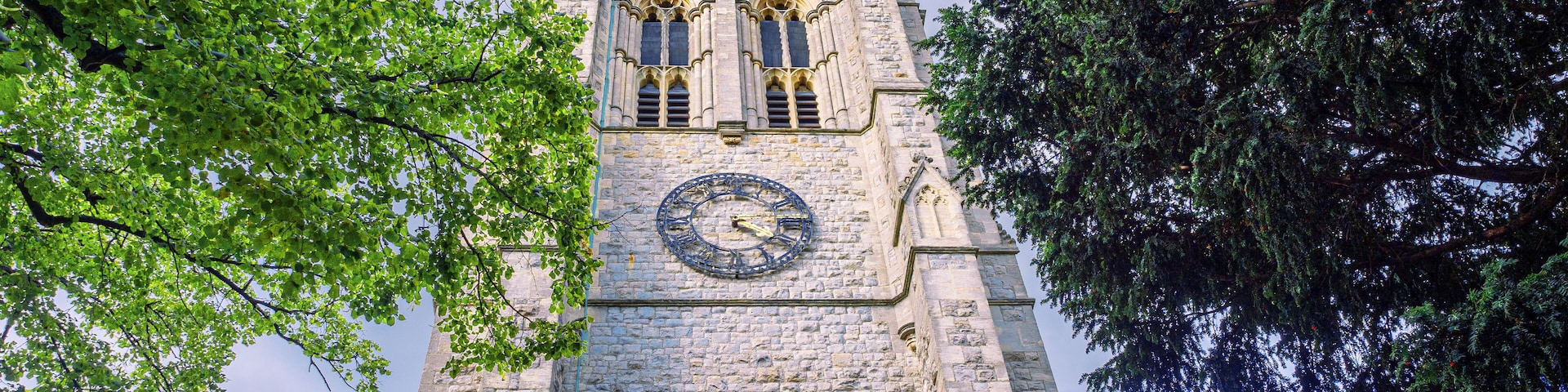 A tall stone tower with a clock, surrounded by trees.