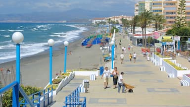 A coastal promenade with a beach, ocean waves, and a row of buildings.