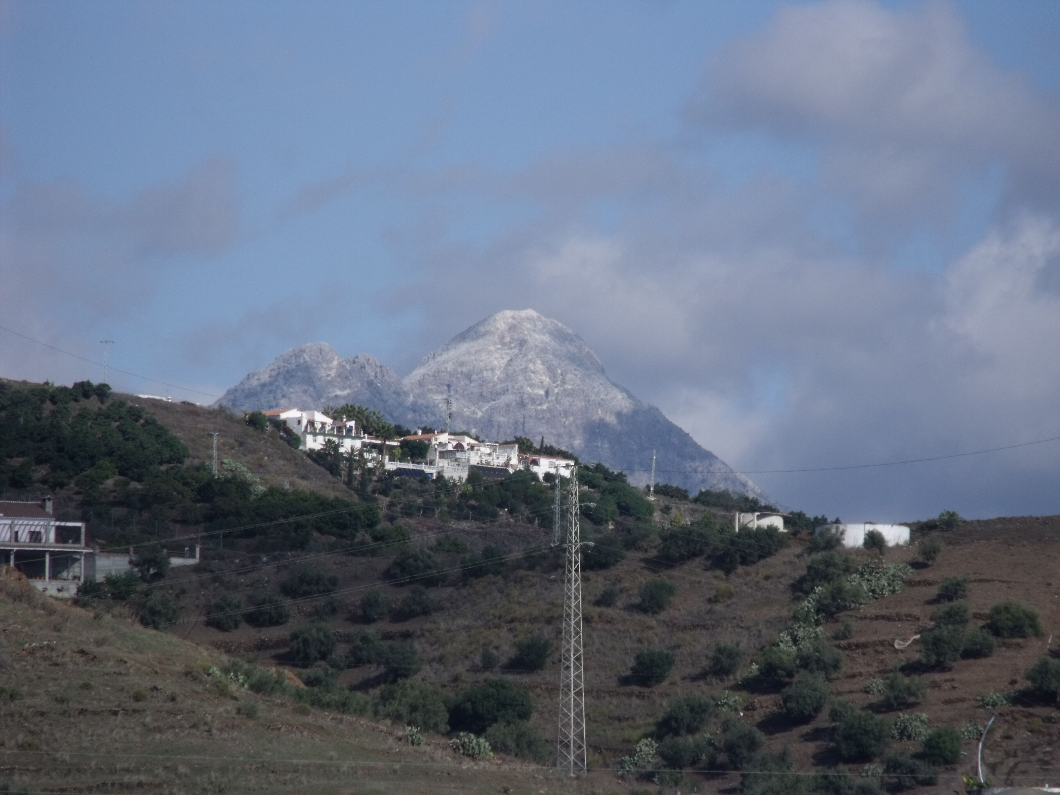 A mountainous landscape with a village on a hillside, power lines, and a clear sky.