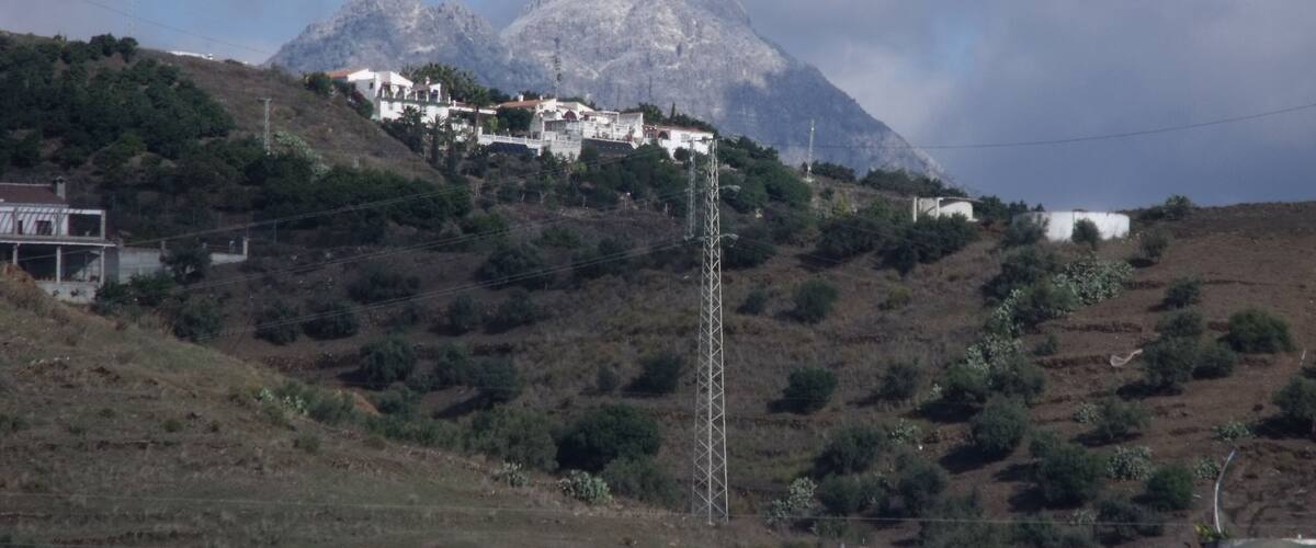 A mountainous landscape with a village on a hillside, power lines, and a clear sky.