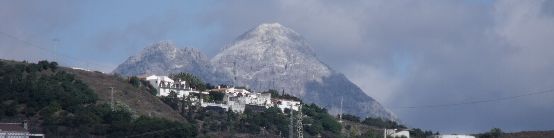 A mountainous landscape with a village on a hillside, power lines, and a clear sky.