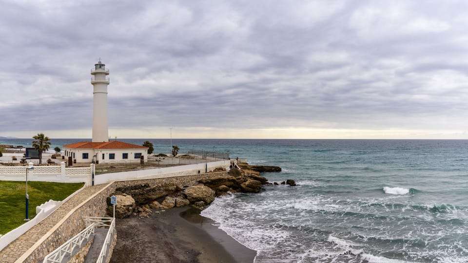 A coastal lighthouse, rocky shoreline, and a clear view of the ocean.