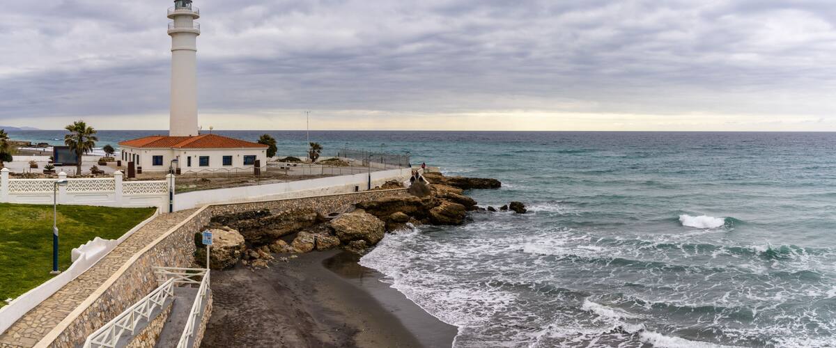 A coastal lighthouse, rocky shoreline, and a clear view of the ocean.
