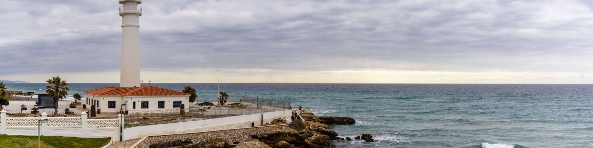 A coastal lighthouse, rocky shoreline, and a clear view of the ocean.