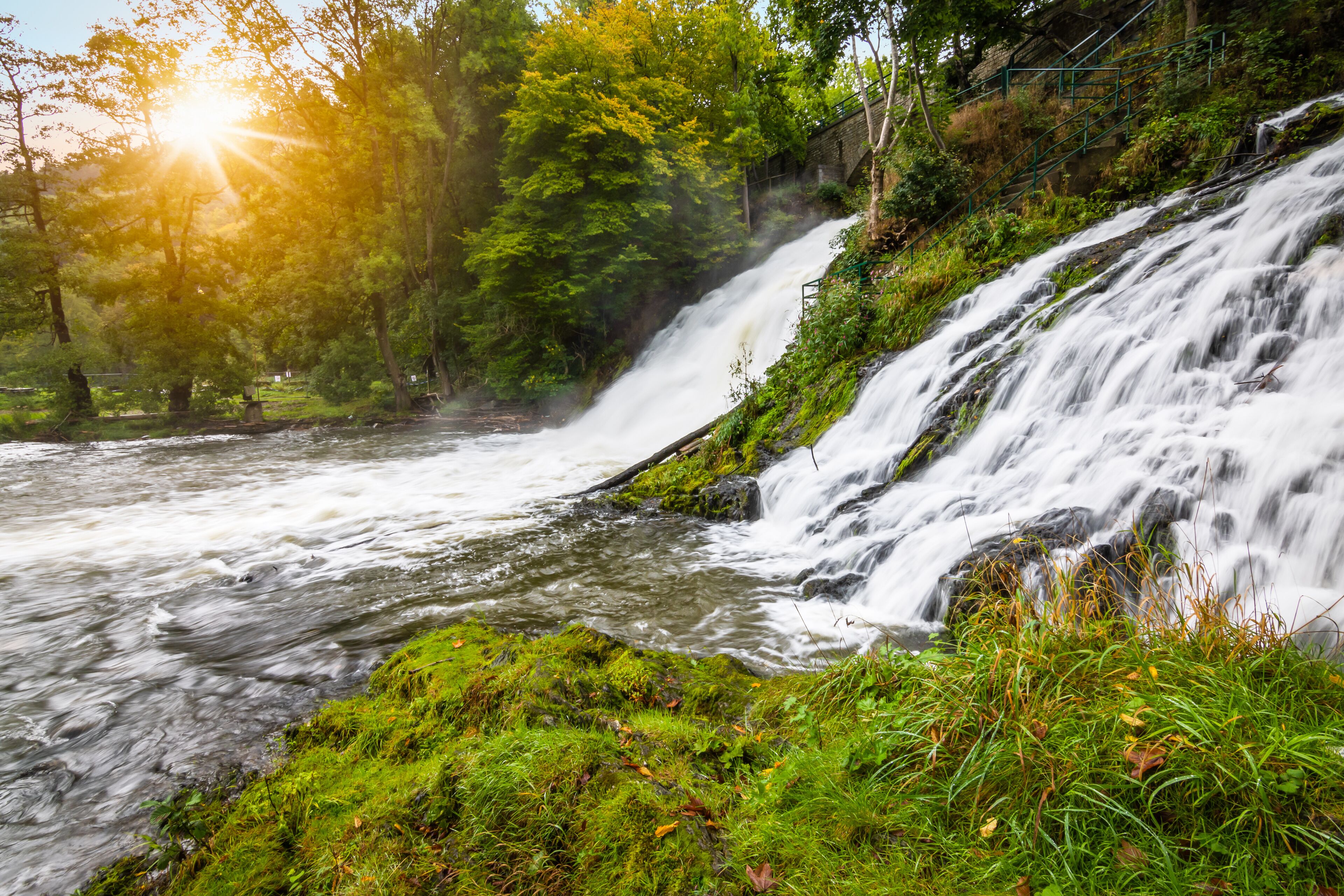 A waterfall cascading over rocks, surrounded by lush greenery and a forested area.