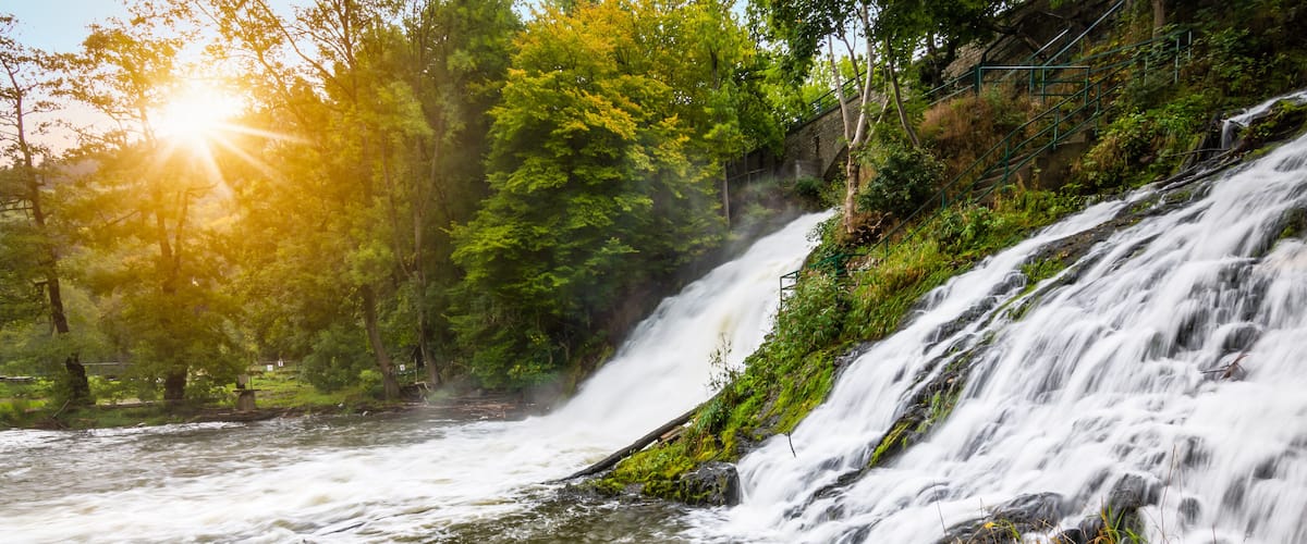 A waterfall cascading over rocks, surrounded by lush greenery and a forested area.