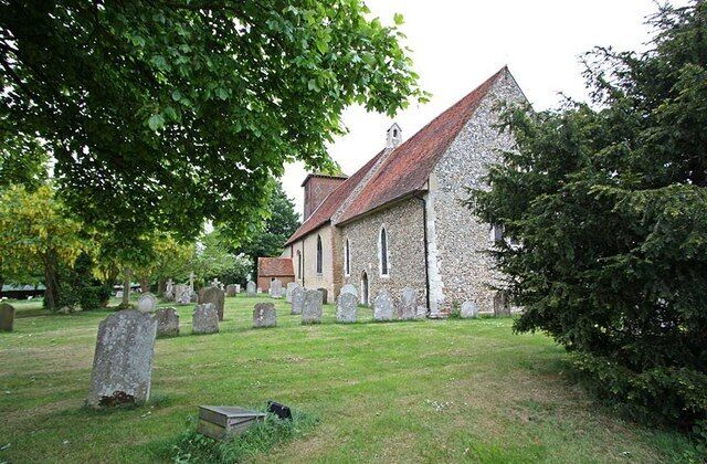 A stone church with a red roof surrounded by gravestones in a cemetery.