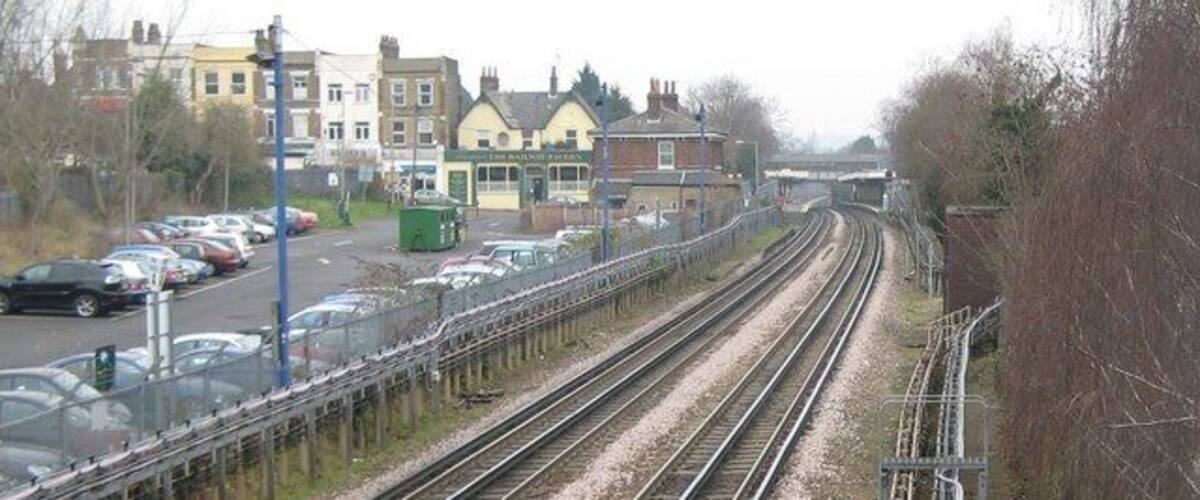 Railway tracks, a road with cars, and residential buildings in the background.