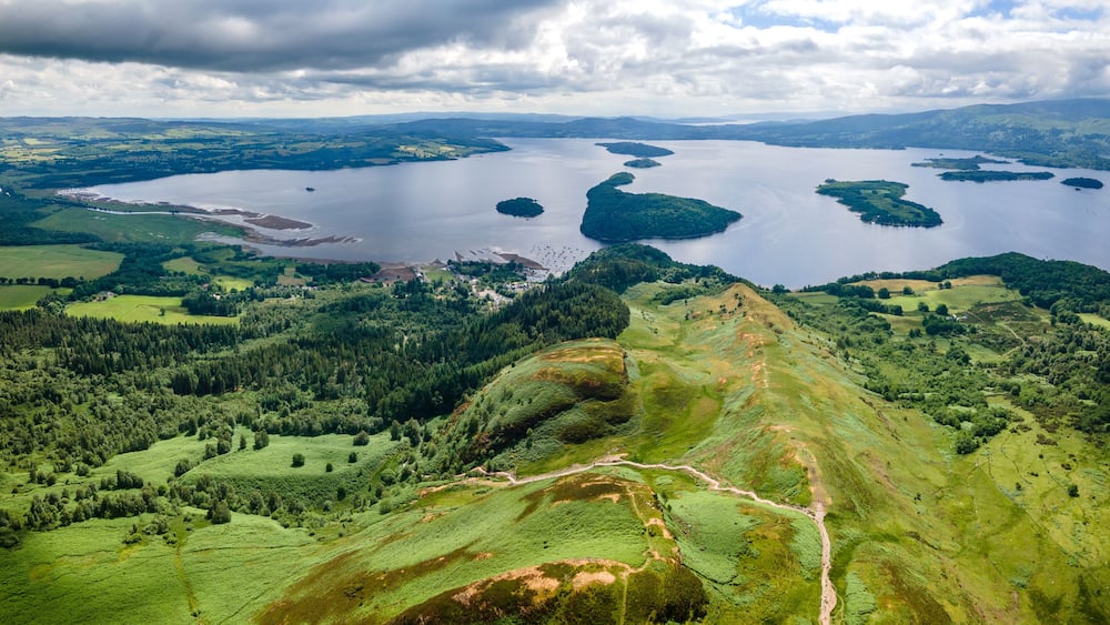A vast lake surrounded by lush green hills and a cloudy sky.