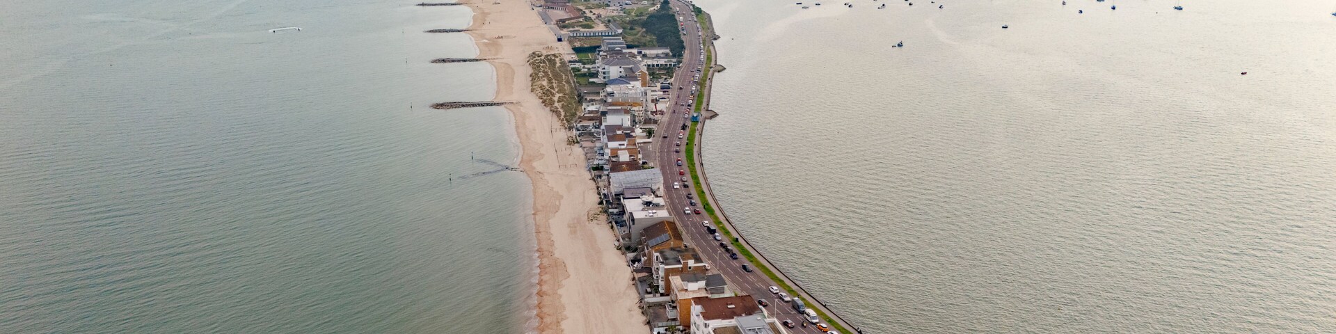 Vista aérea de uma cidade costeira com uma praia extensa, área urbana densa e um porto com muitos barcos.