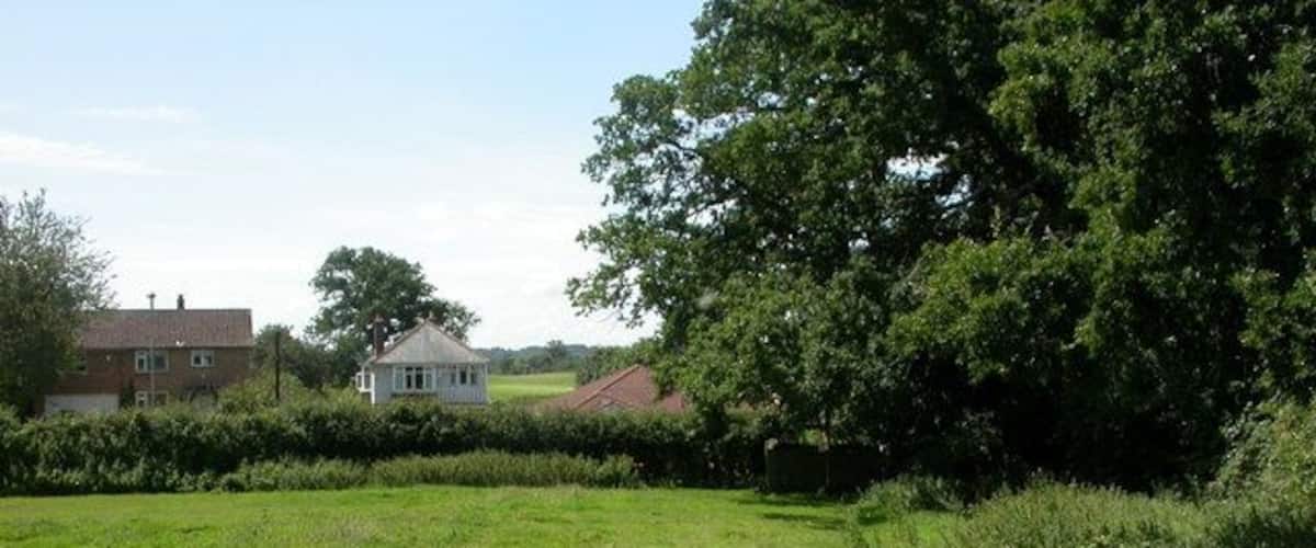 A grassy field with a house and trees in the background.