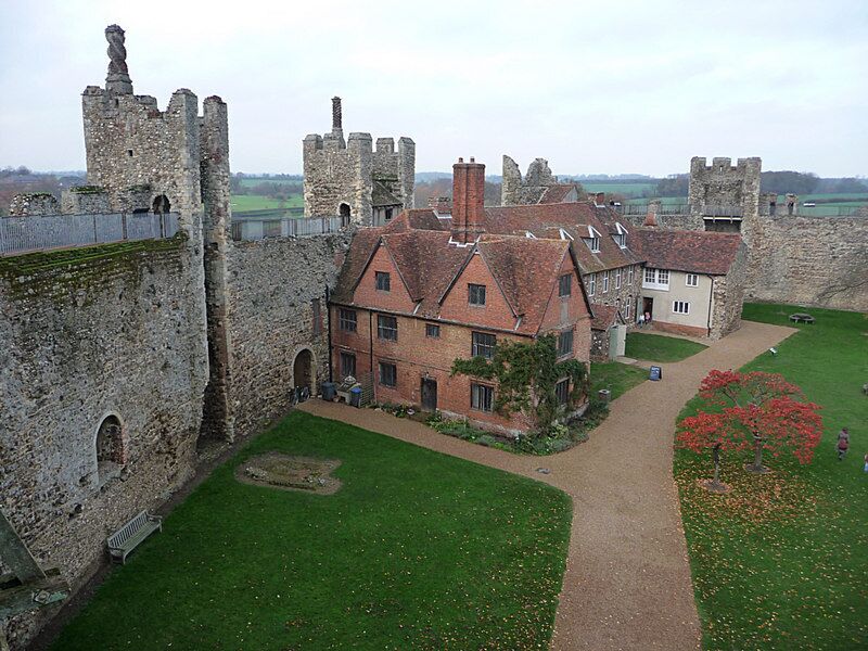 A historic castle with stone walls and a red-roofed building in the foreground.