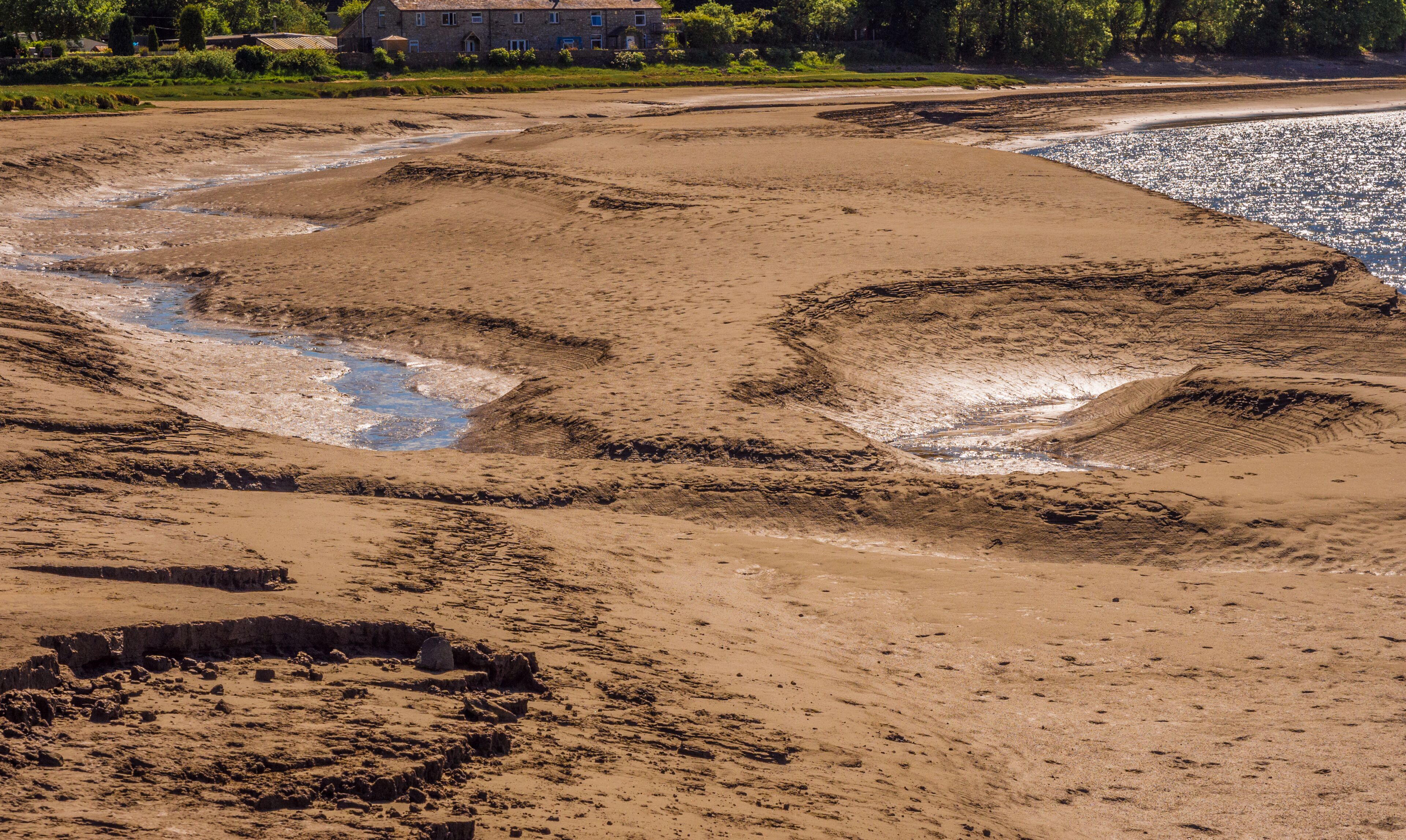 A sandy beach with water channels and a building in the background.