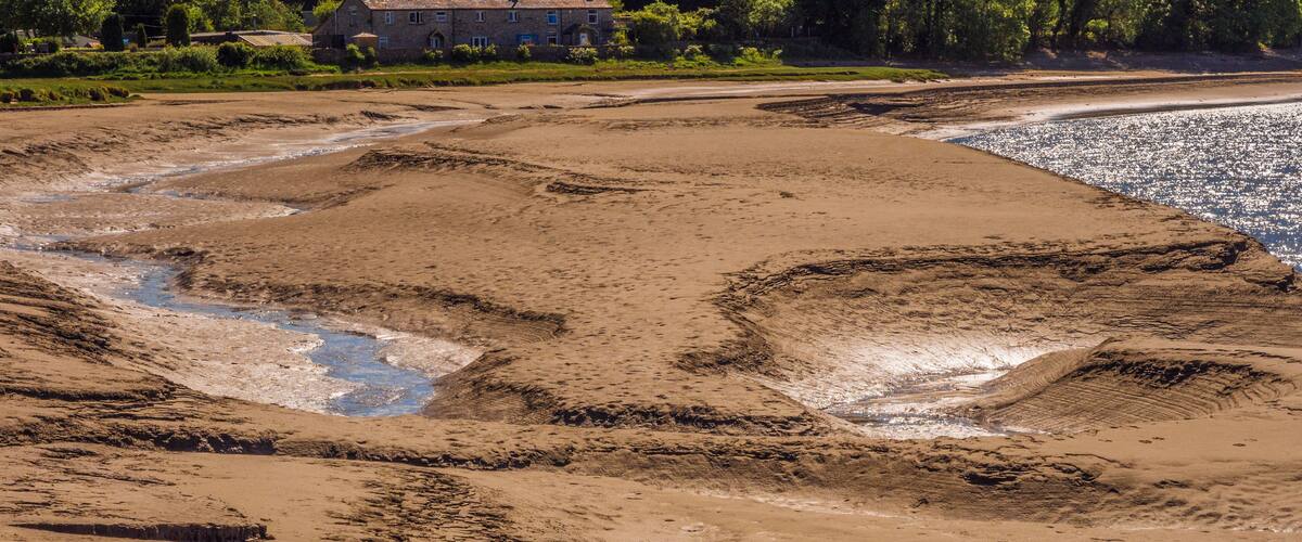 A sandy beach with water channels and a building in the background.