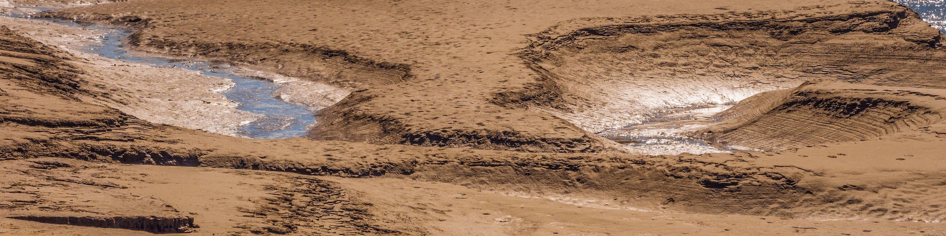 A sandy beach with water channels and a building in the background.