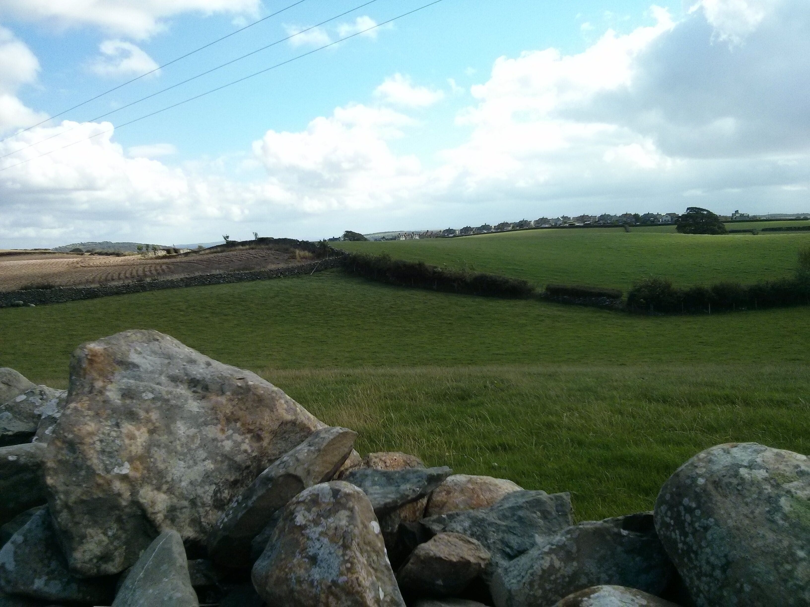 A rural landscape with green fields, stone walls, and a distant village.