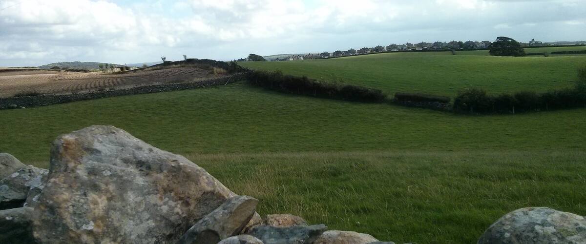 A rural landscape with green fields, stone walls, and a distant village.