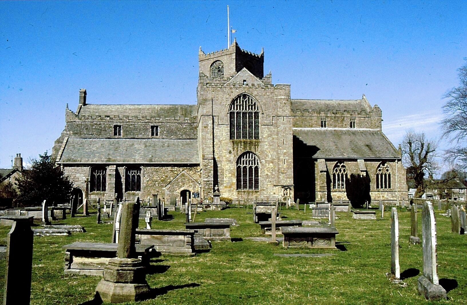 A historic church with a tall tower and arched windows, surrounded by a cemetery with headstones.