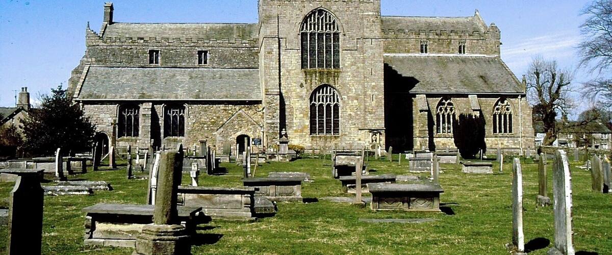 A historic church with a tall tower and arched windows, surrounded by a cemetery with headstones.