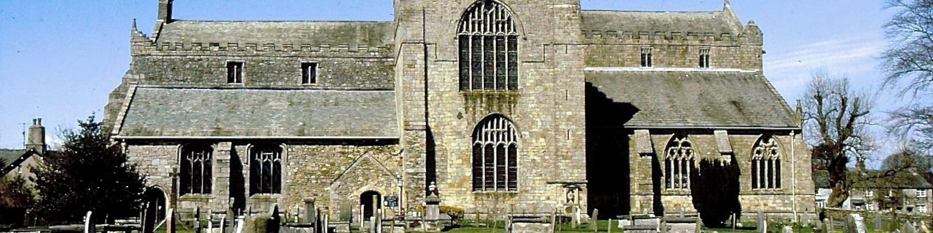 A historic church with a tall tower and arched windows, surrounded by a cemetery with headstones.