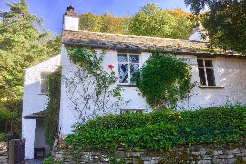 A white house with a stone wall and a stone chimney.