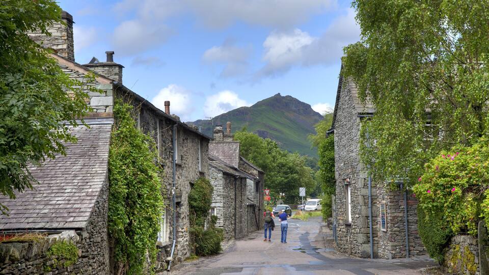 A narrow stone street flanked by traditional stone buildings, with a mountain in the background.