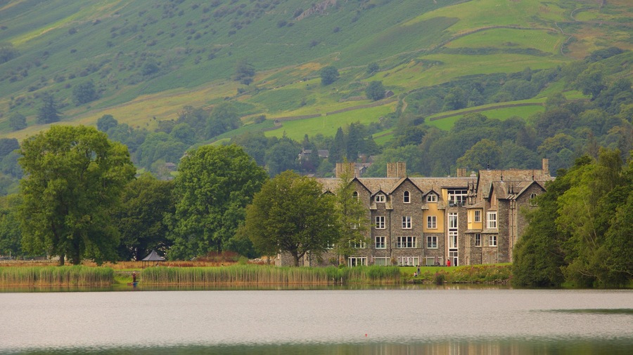 A historic stone building with multiple chimneys, surrounded by lush greenery and a calm lake.